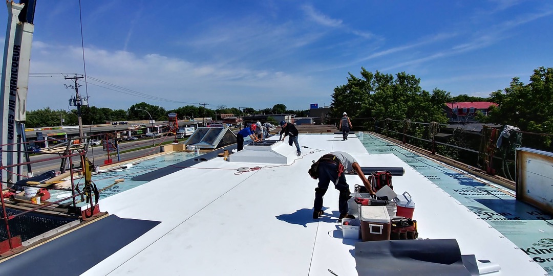 Équipe de spécialistes couvreurs posant une membrane TPO sur un toit plat