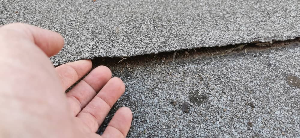 Une main montre une fissure de la membrane où l'eau peut s'infiltrer sur un toit plat