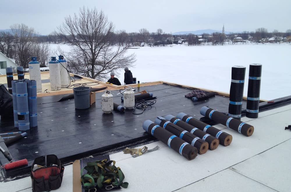 Installation en cours d'une membrane élastomère sur toit plat résidentiel