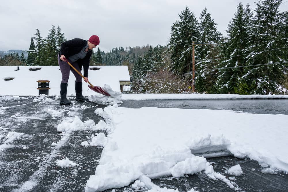 Une femme déneige un toit plat à la pelle