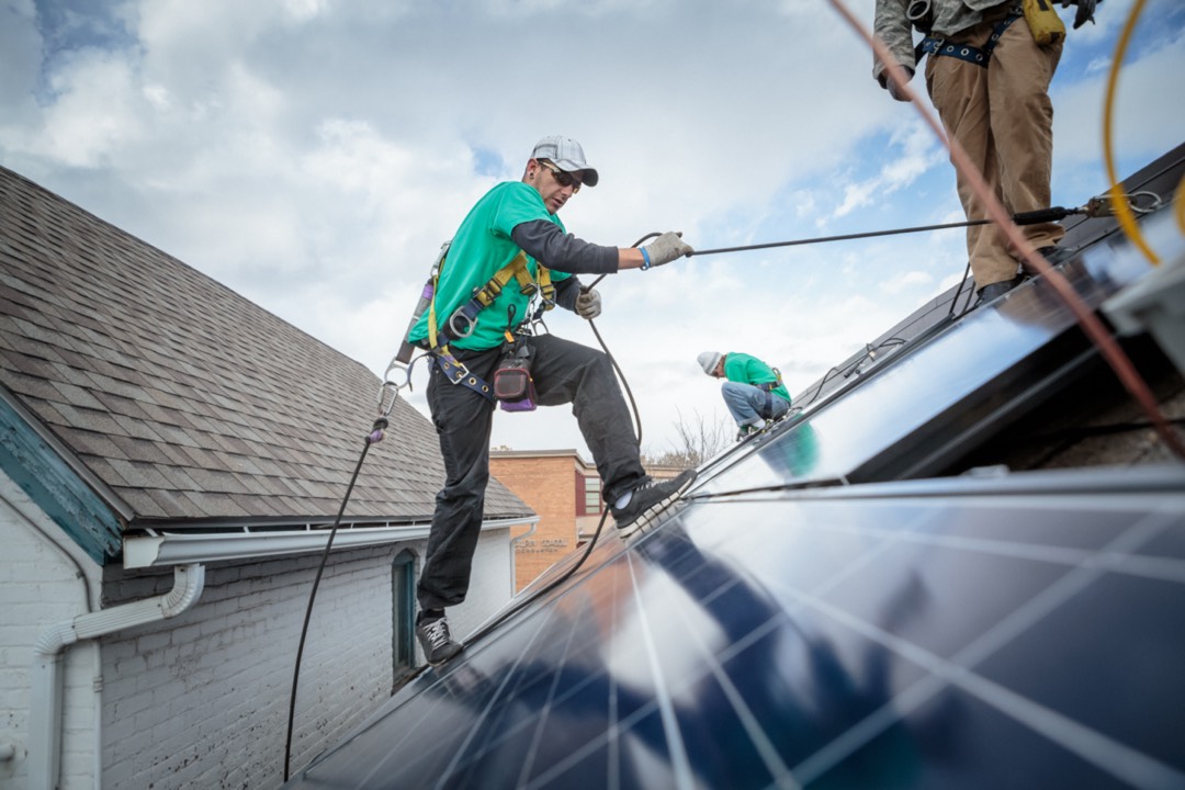 A roofer climbing on a solar panel using a safety harness.