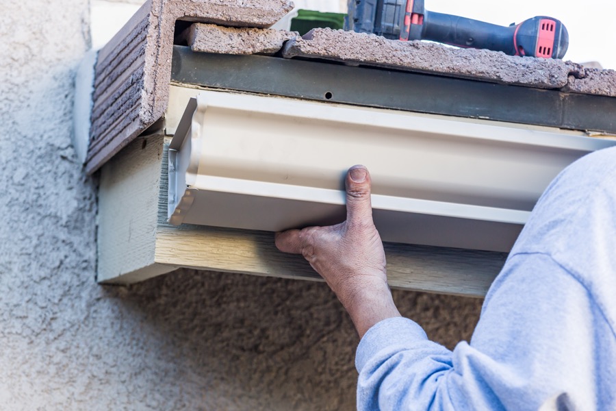 Worker attaching an aluminum gutter to the fascia of a house.