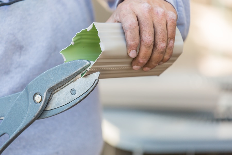 Worker cutting the profile of an aluminum gutter with heavy shears.