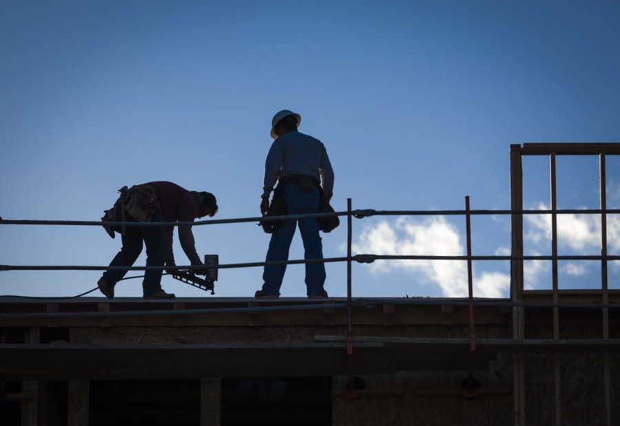 Silhouette of builders installing a guardrail on a roof.