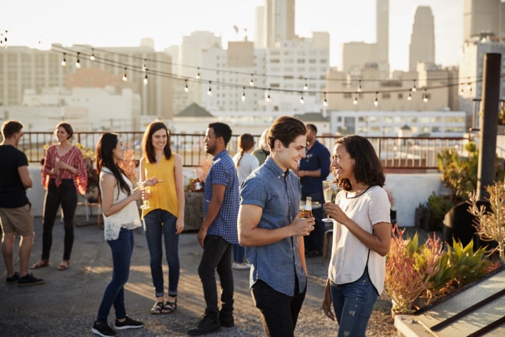 Friends gathered on rooftop terrace for party with city skyline in background.