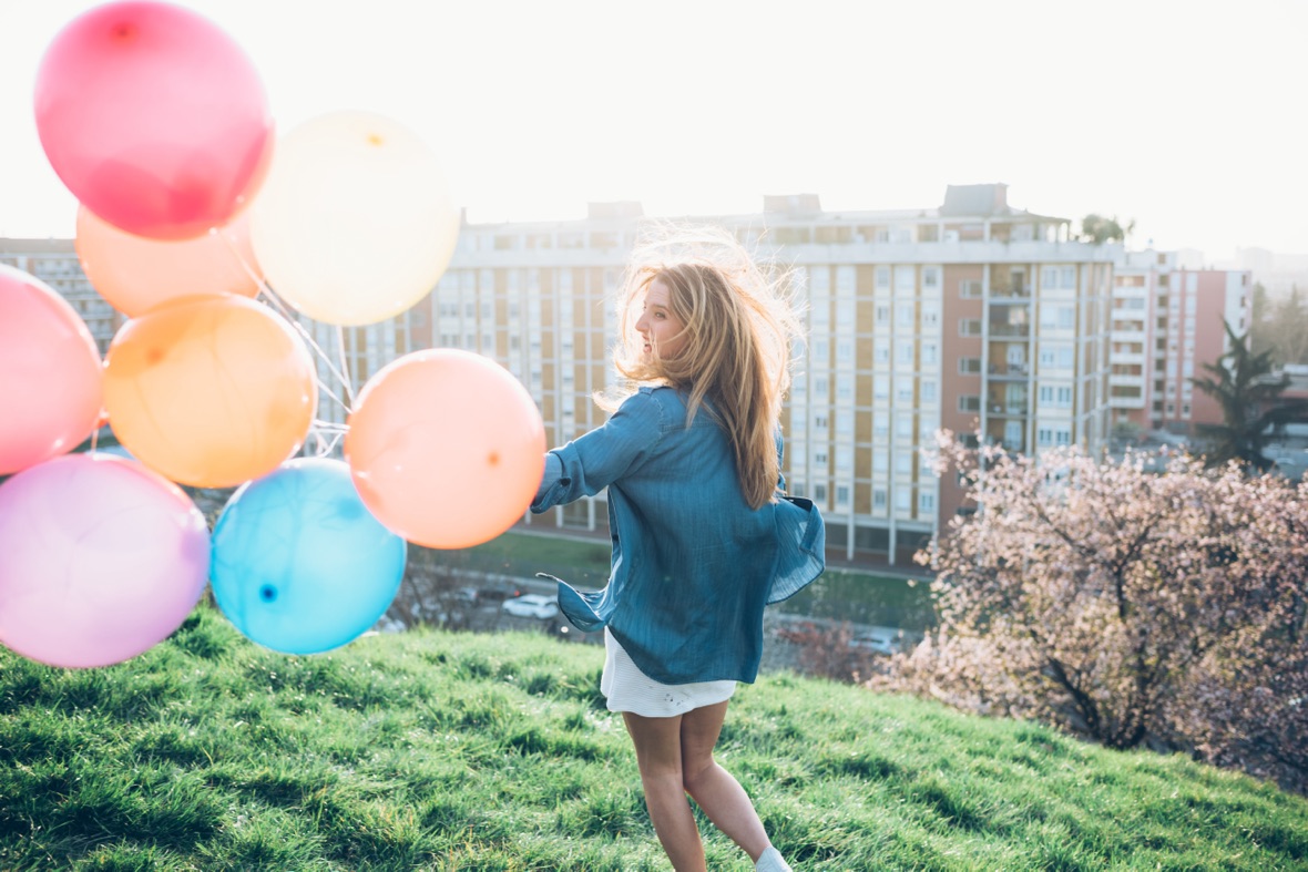 Young woman standing on a green roof, holding helium balloons.