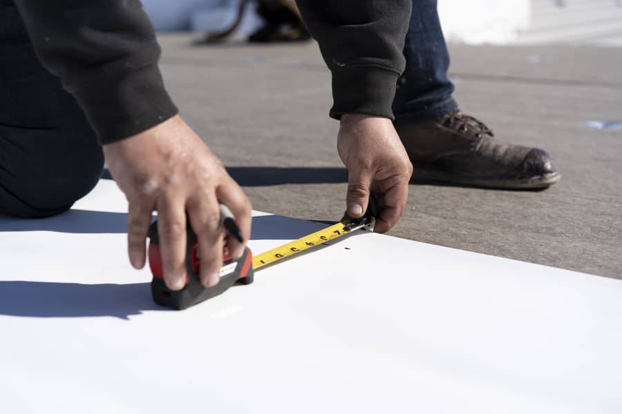 A roofer measures the width of a strip of TPO membrane.
