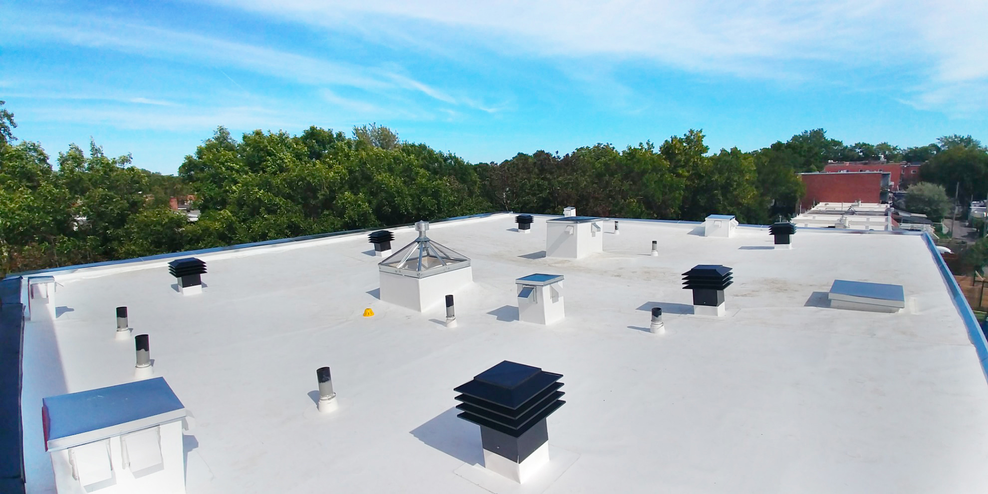 White membrane flat roof with multiple vents and skylights on a sunny summer day in Montreal.