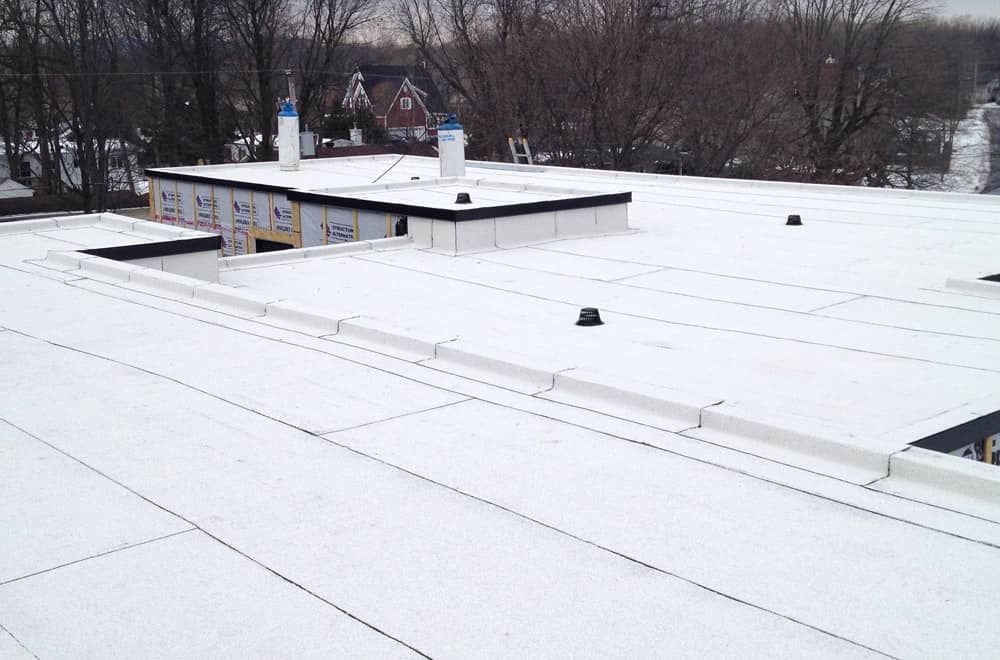 Flat roof with white TPO membrane installed in winter, with ventilation outlets and a rooftop structure under construction.